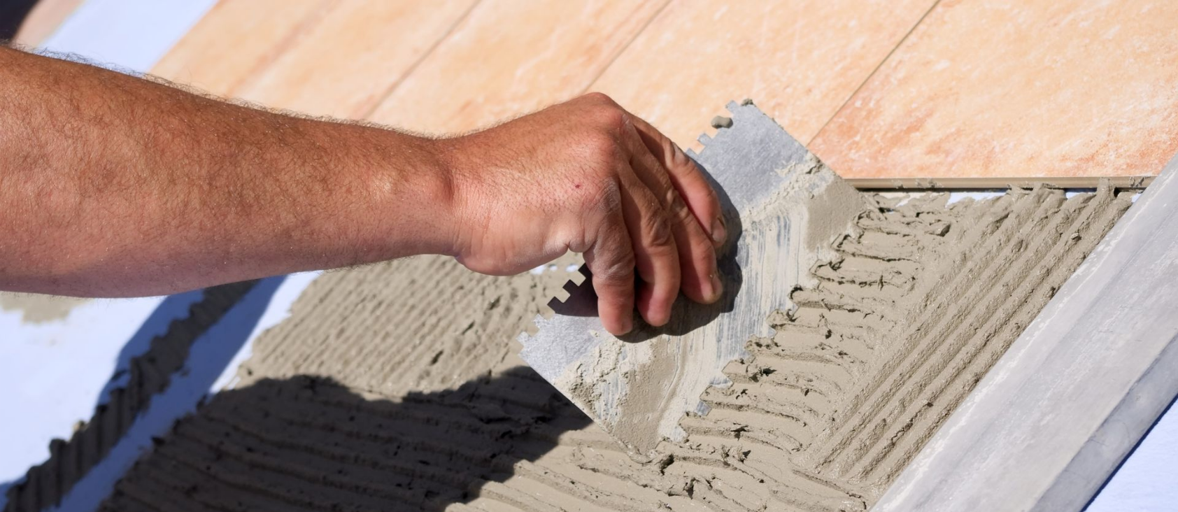 Personne utilisant une truelle pour appliquer du mortier sur une surface, en préparation de la pose de carrelage.