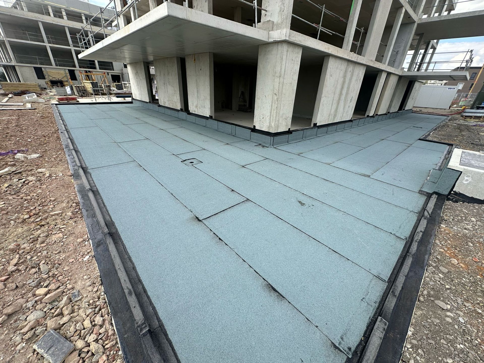 Toit plat à la surface bleu-gris en construction à côté d'un bâtiment.