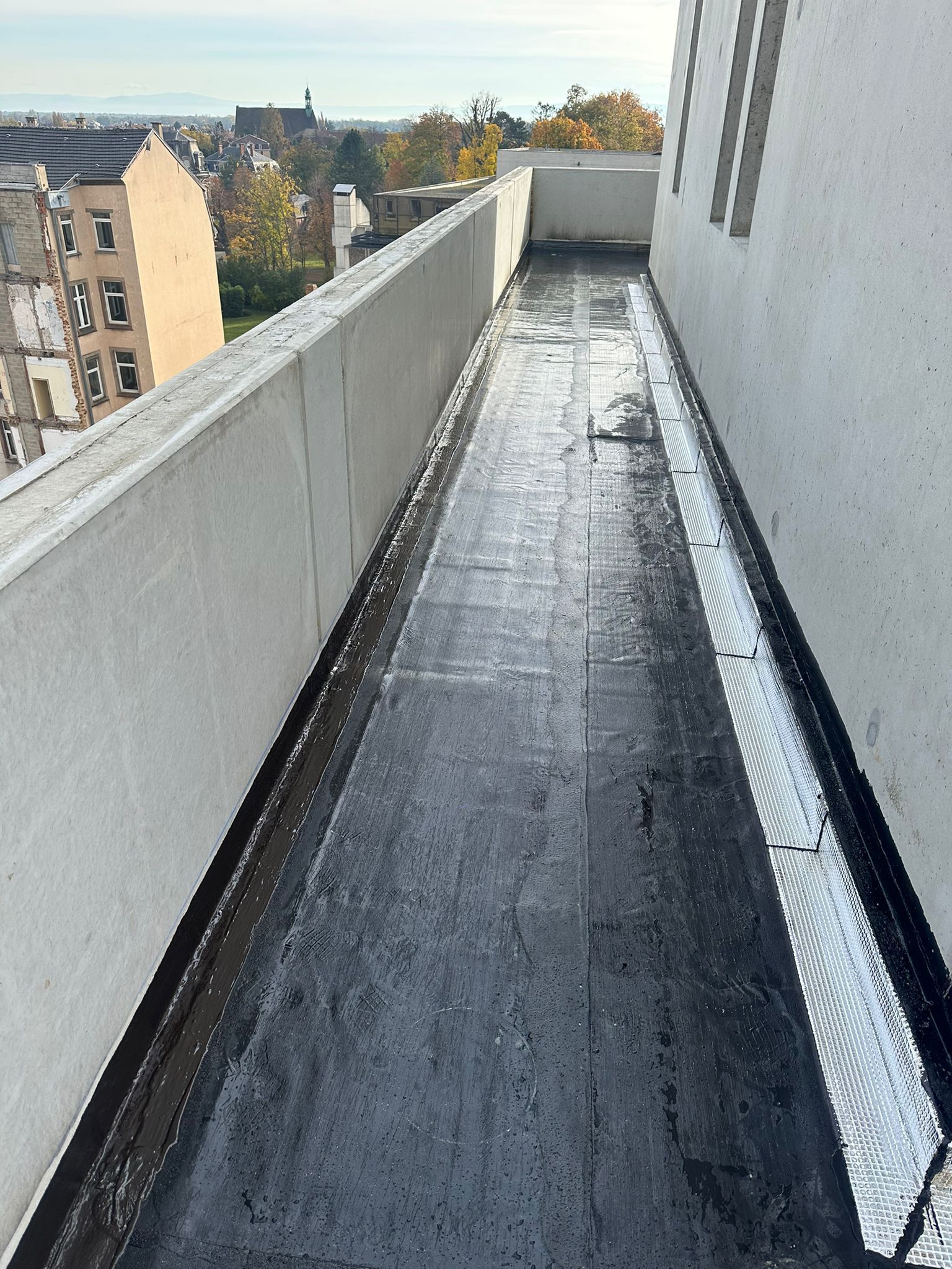 Un couvreur en salopette bleue utilise un chalumeau pour chauffer la surface d'un toit plat ; des flammes orange sont visibles.