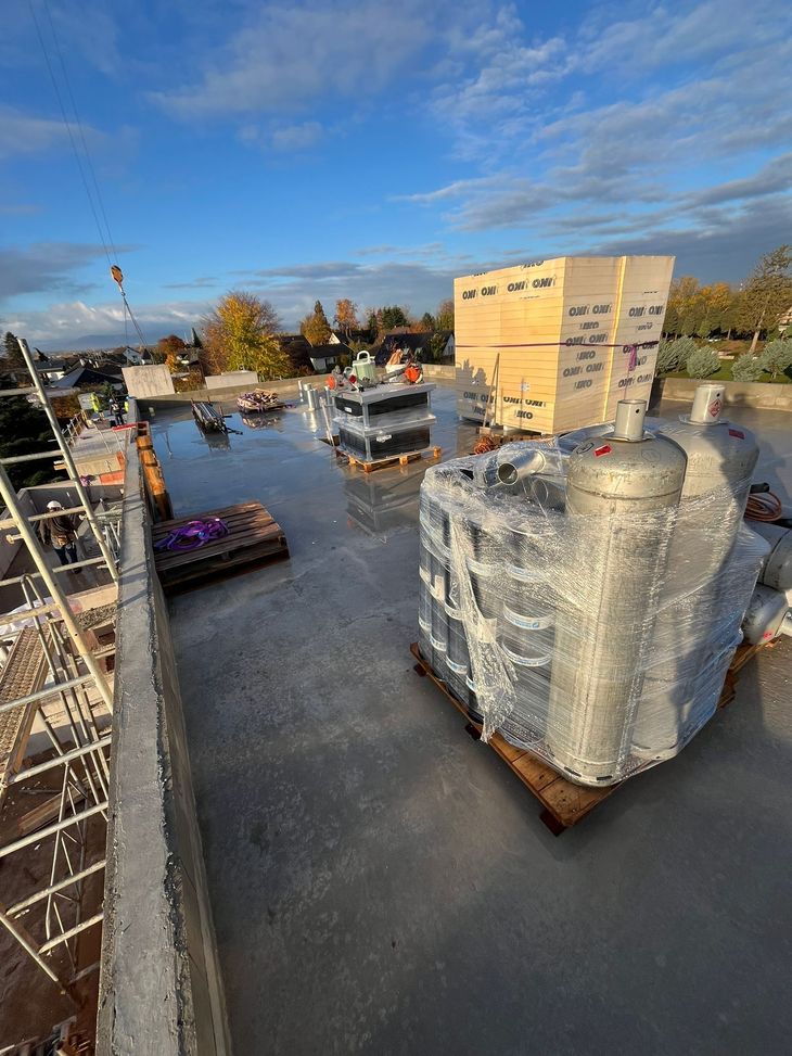 Chantier de construction de toiture avec des palettes de matériaux de construction sous un ciel bleu.
