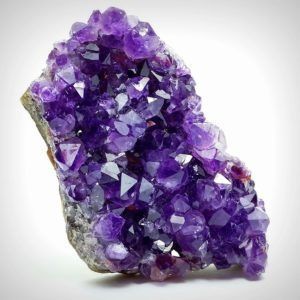 Lila Amethyst-Kristallcluster auf einem grauen Felssockel.