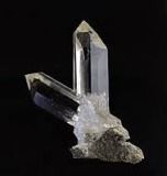 Klarer Quarzkristallcluster auf einem grauen Felssockel vor schwarzem Hintergrund.