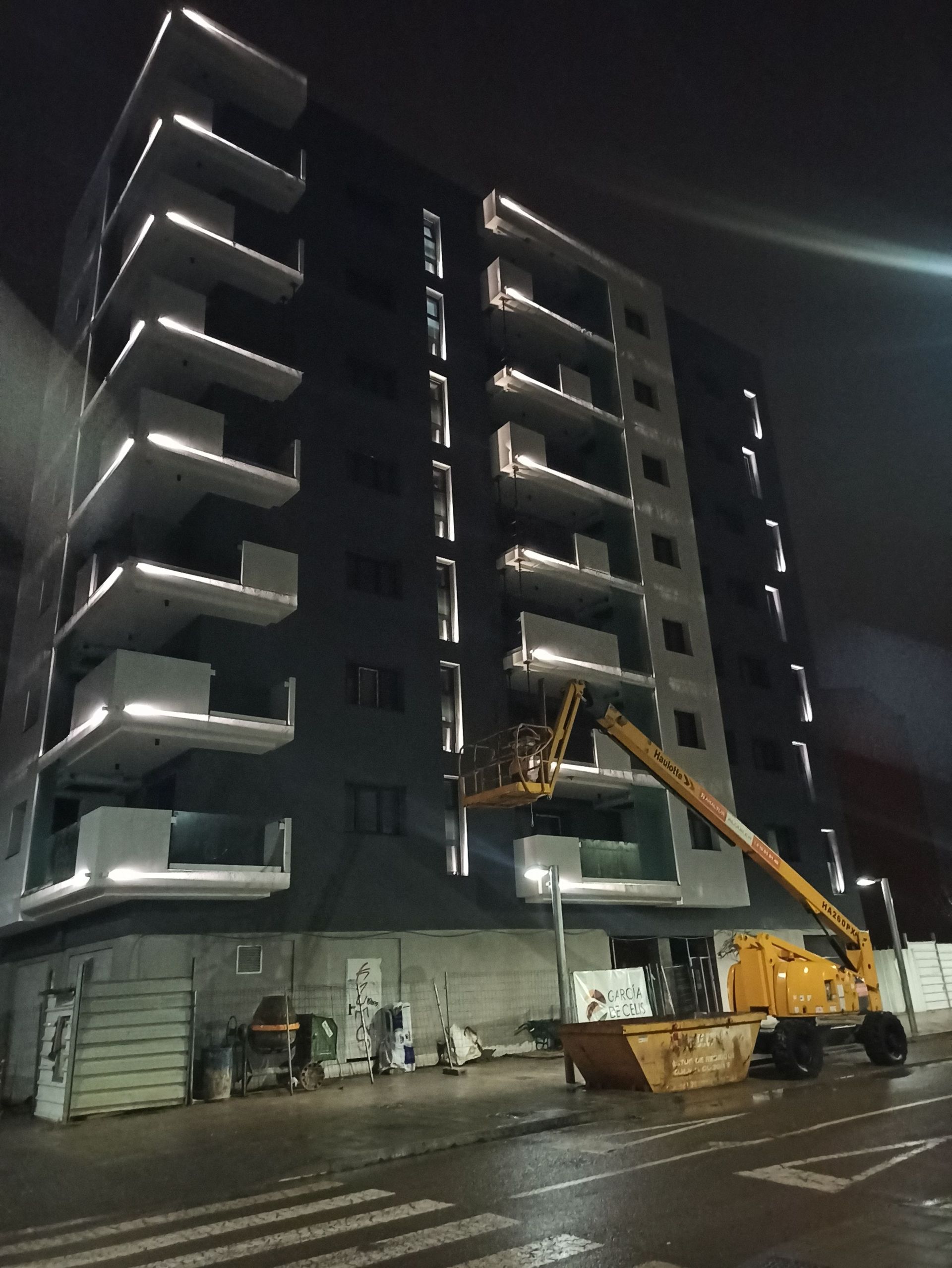 Un gran edificio con una grúa delante por la noche.