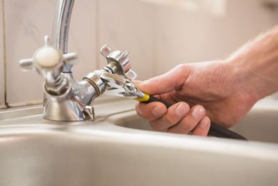 Wasserhahn von Waschbecken wird mit Zange von Person gedreht