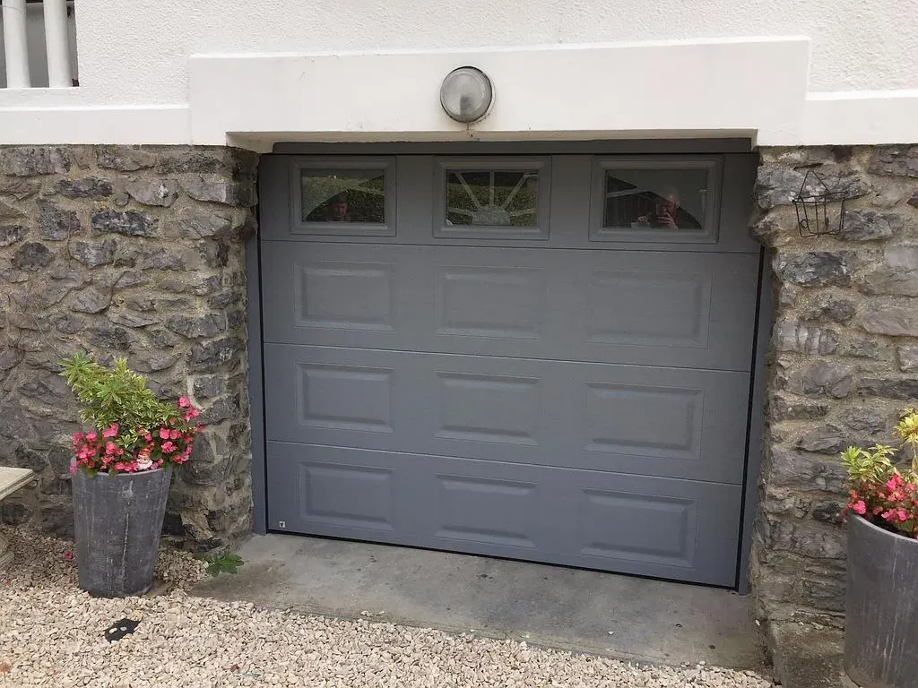 Porte de garage grise avec 2 grands pots de fleurs aux extrémités