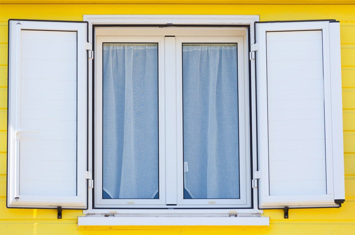 Fenêtre blanche avec volets battants ouvert sur une façade jaune