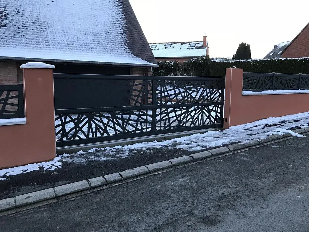 Portail noir ajouré d'une maison vêtue d'une couche de neige
