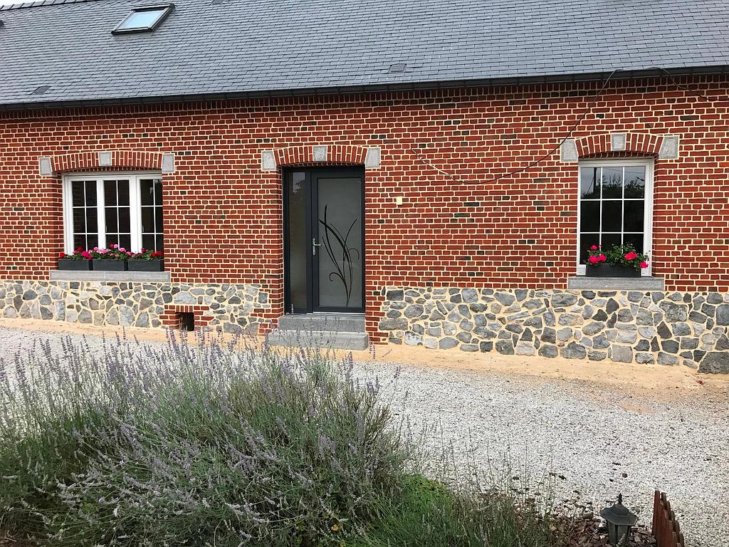 Façade d'une maison en brique avec vitrophanie sur la porte d'entrée noire et 2 fenêtres blanches