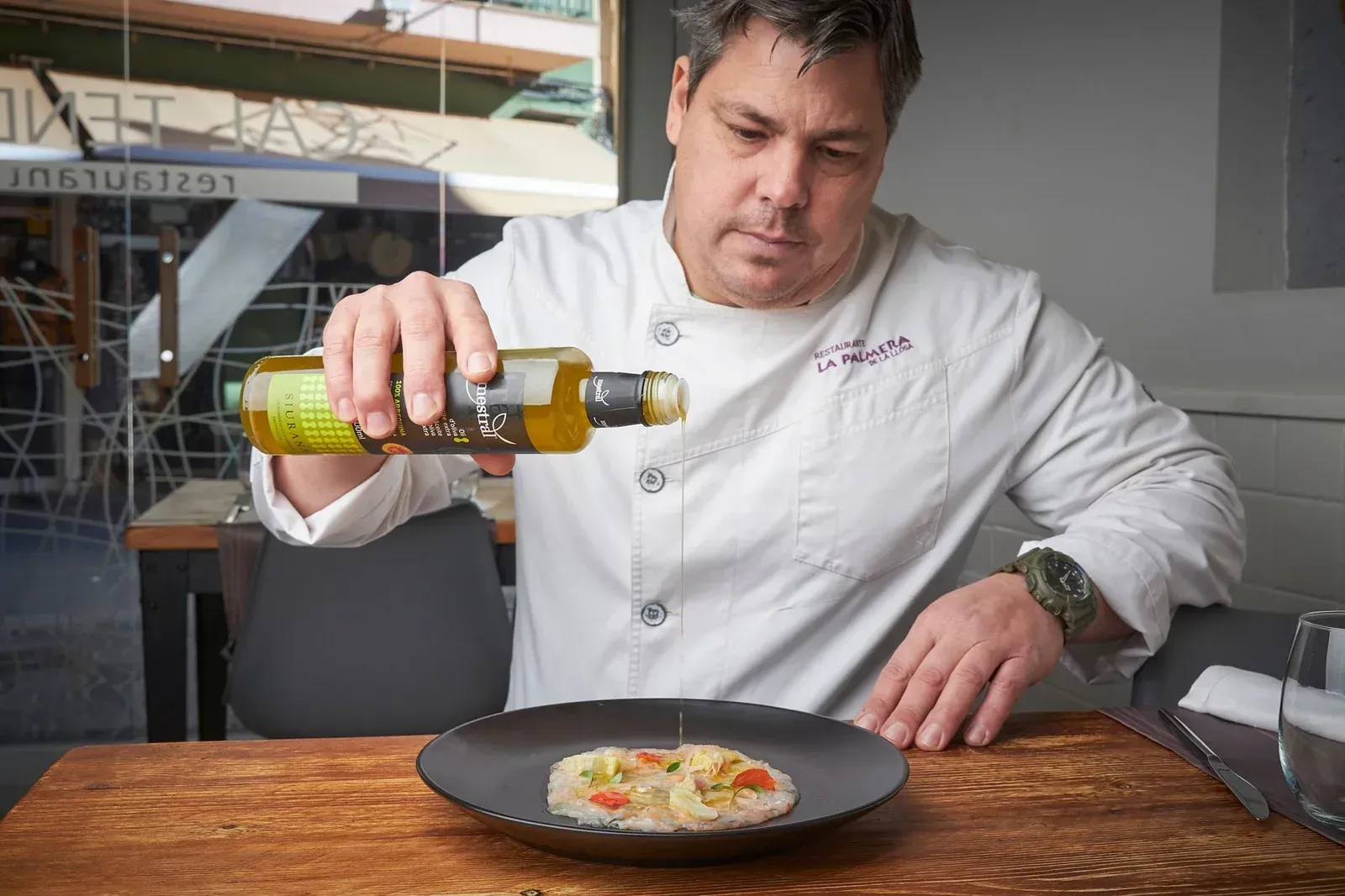 Chef rociando aceite de oliva sobre un plato en una cocina.