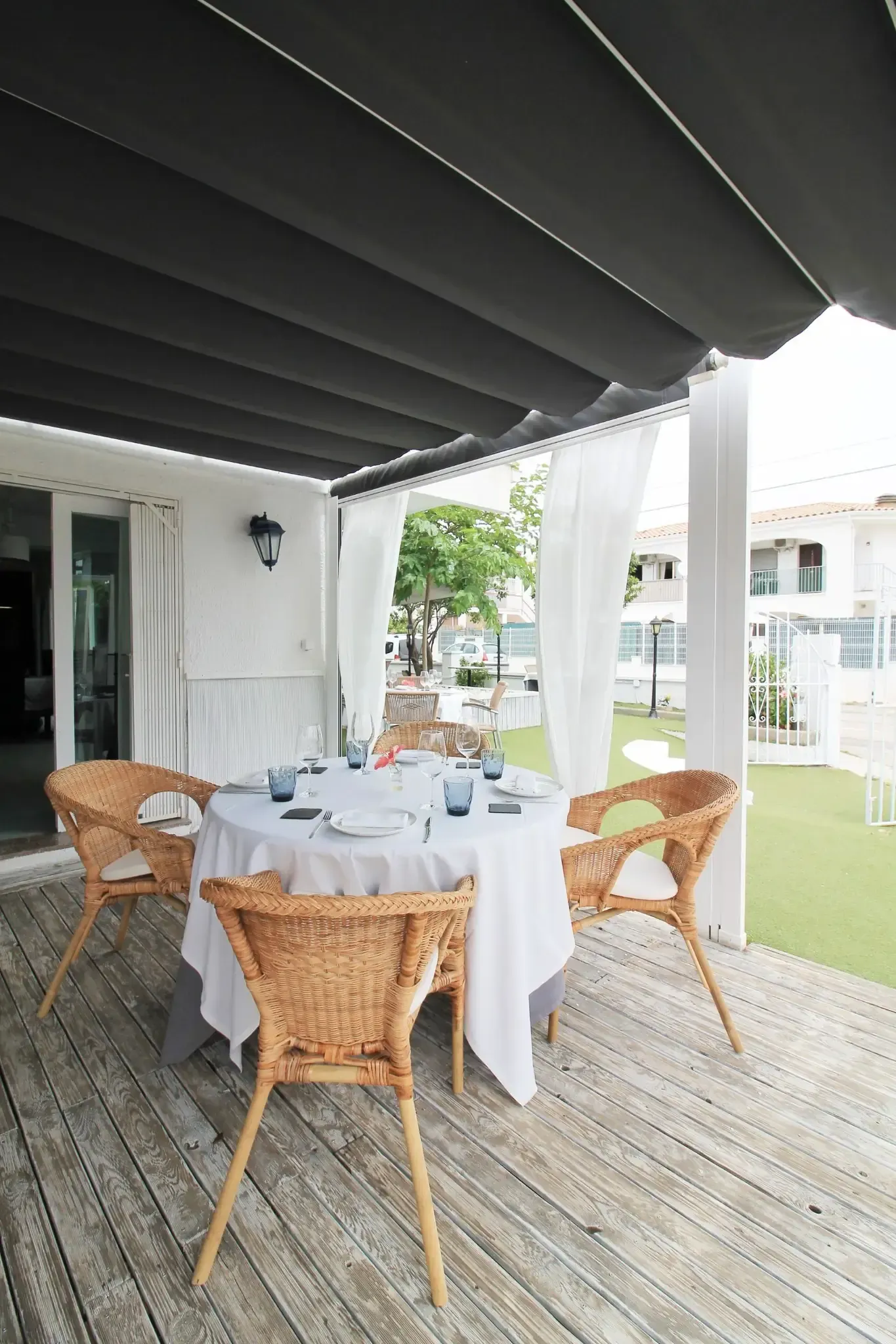 Patio cubierto con sillas de mimbre y una mesa redonda dispuesta para comer en una terraza de madera.