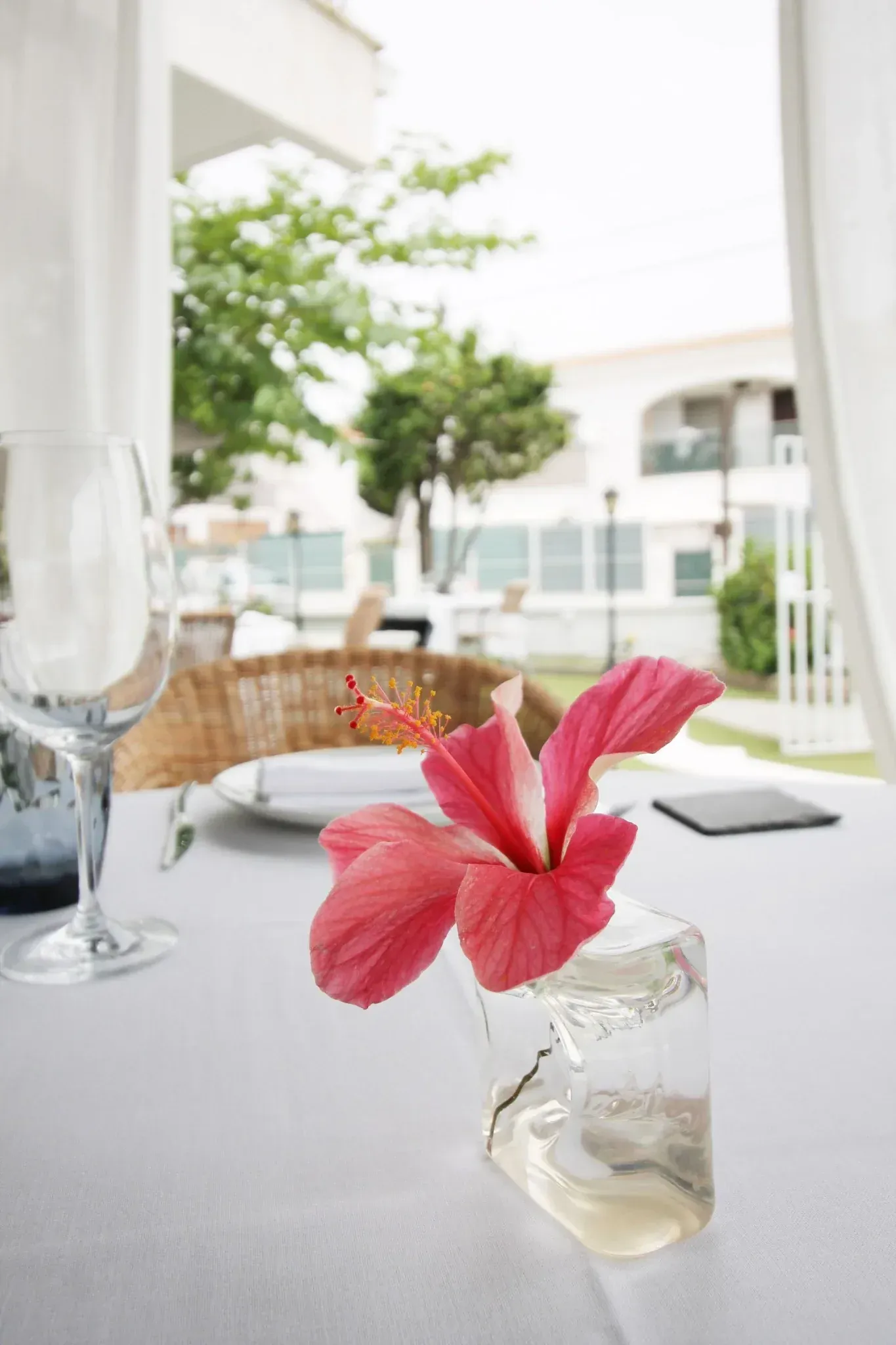 Prepara la mesa del comedor con copas de vino, servilletas dobladas y un centro de mesa floral rosa.