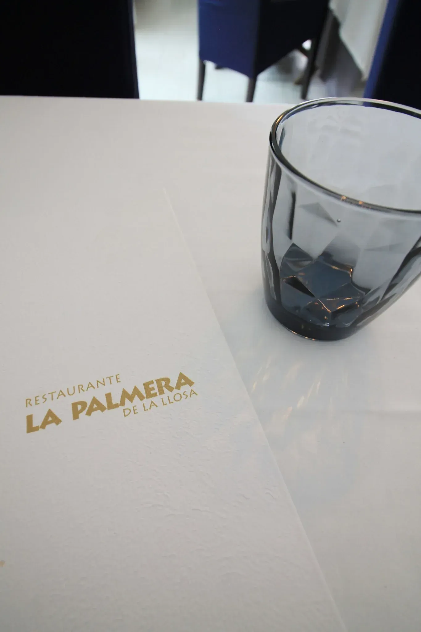 Mesa de restaurante con un vaso azul y una servilleta con la etiqueta “La Pamera”.