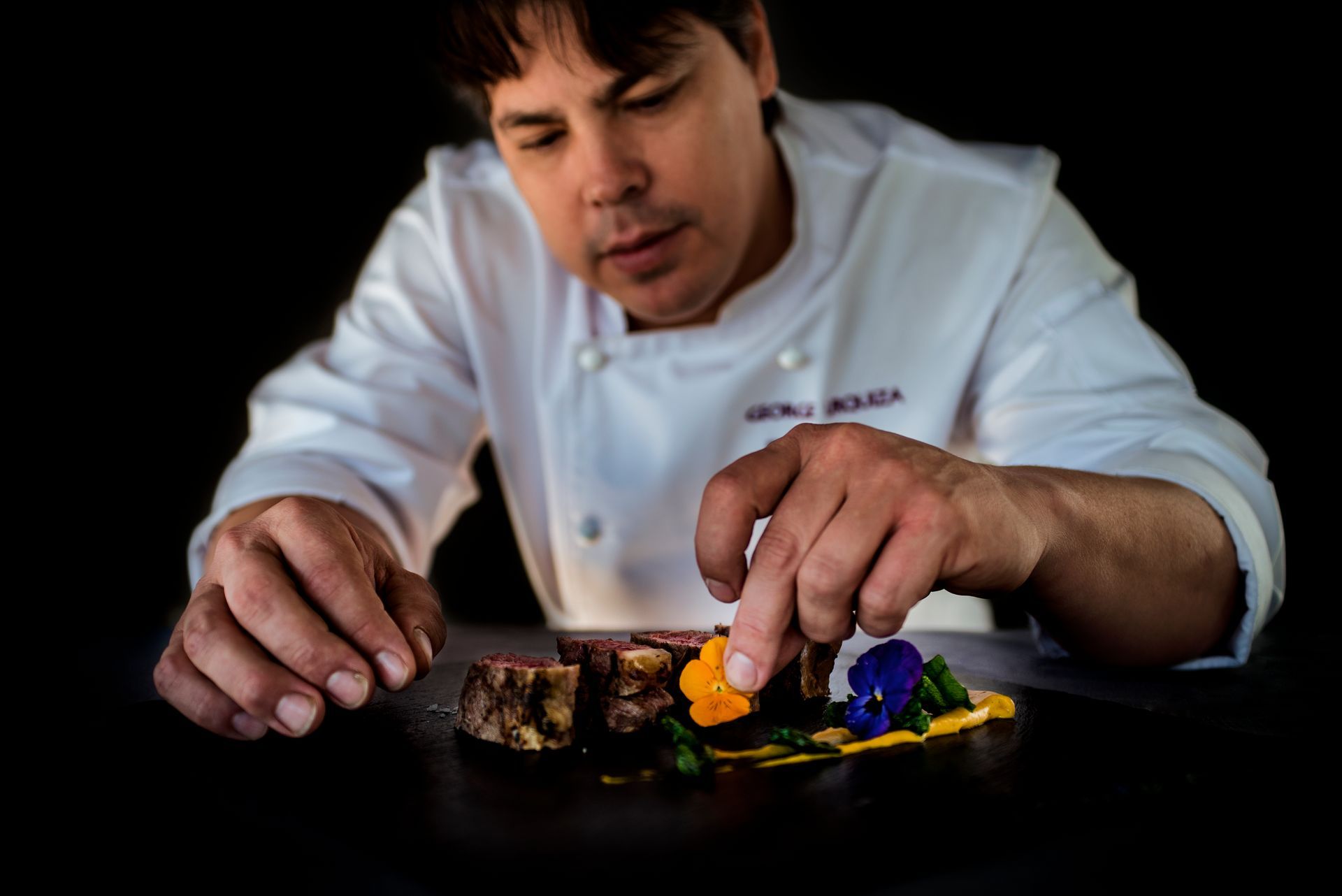 El chef dispone platos coloridos sobre una mesa oscura, centrándose en la presentación.