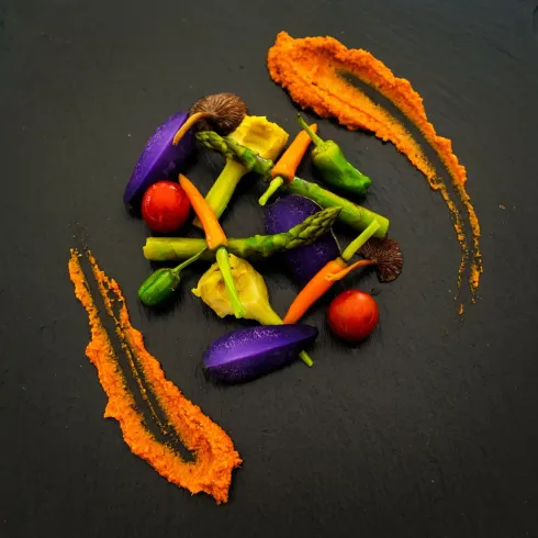Verduras coloridas dispuestas artísticamente en un plato oscuro con vetas de salsa naranja.