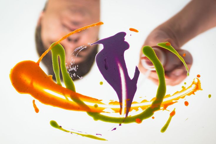 Logotipo abstracto y colorido con remolinos de pintura naranja, verde y morada sobre un fondo blanco.