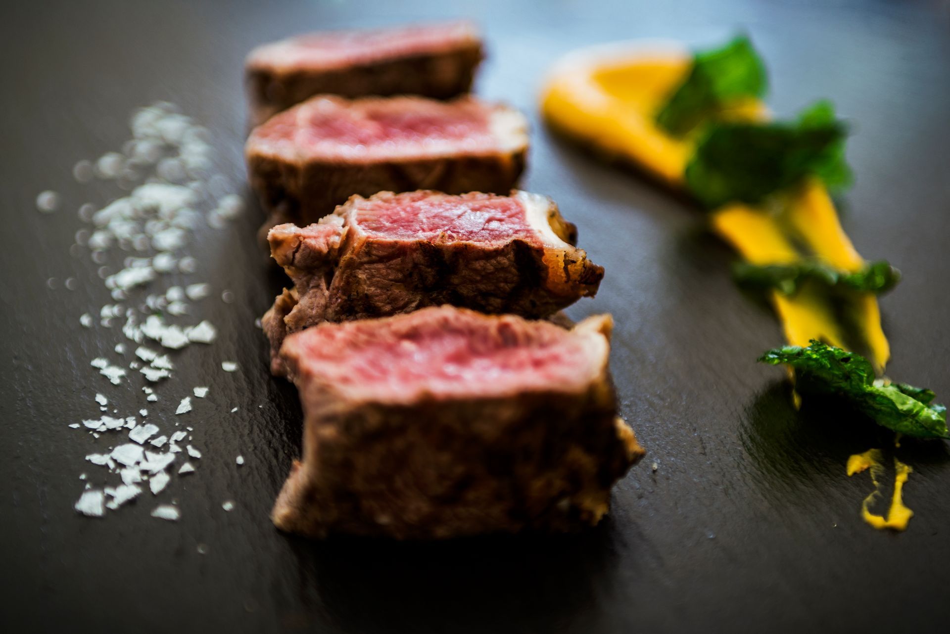 Filete poco hecho en rodajas sobre un plato oscuro con sal gruesa y guarnición de limón.