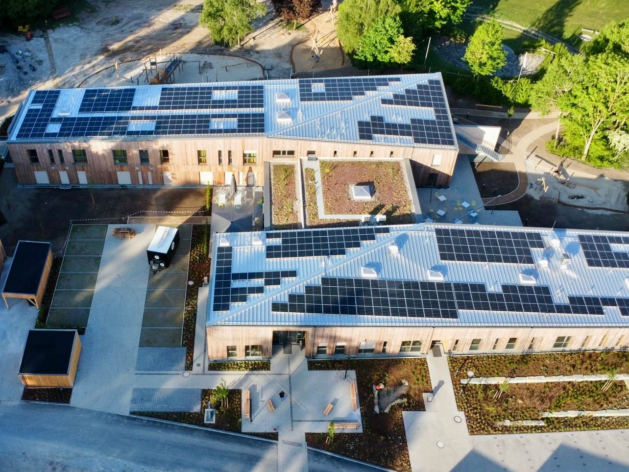 Zweistöckige Backsteingebäude mit Solarmodulen auf den Dächern, einem Gründach und einem zentralen Innenhof.