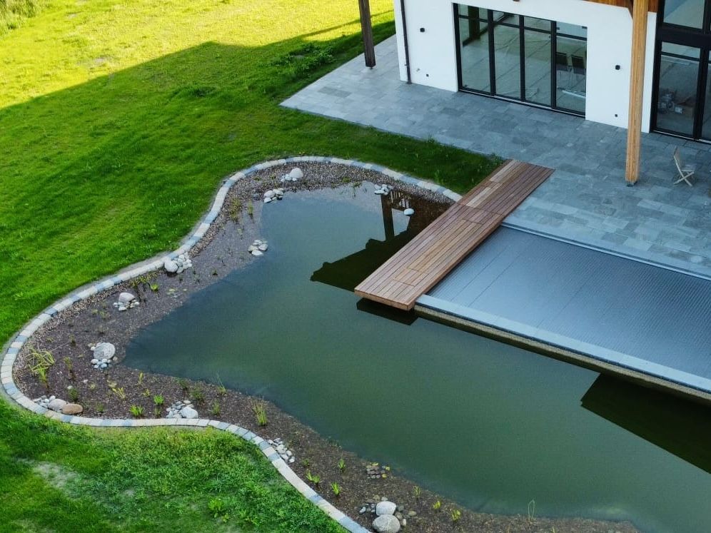Ein modernes Haus mit Teich und Holzbrücke, umgeben von grünem Rasen.