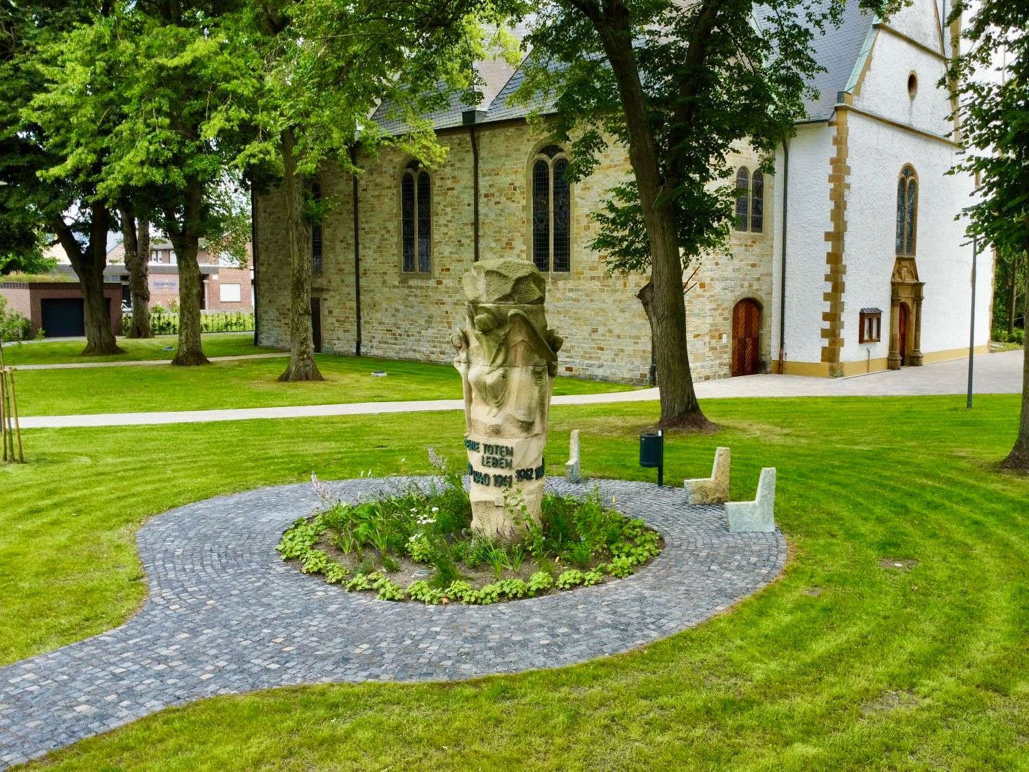 Steindenkmal in einem Garten mit einer Kirche im Hintergrund.