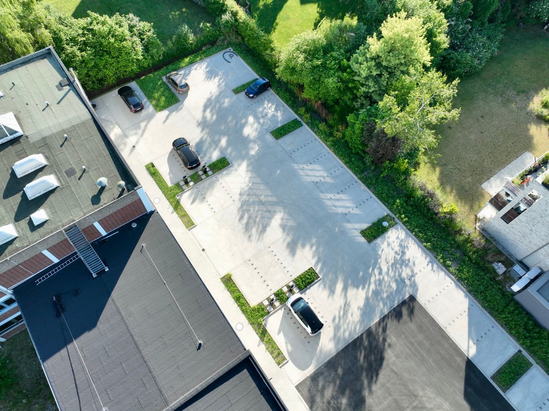 Luftaufnahme eines Parkplatzes mit mehreren geparkten Autos. Betonierter Parkplatz mit Grünflächen, Bäumen und angrenzenden Gebäuden.
