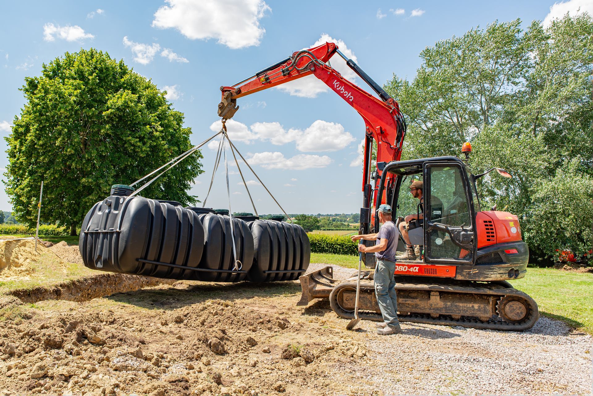 2 ouvriers sur un chantier de viabilisation dont 1 avec qui utilise un engin sur chenille pour entérer une fosse septique
