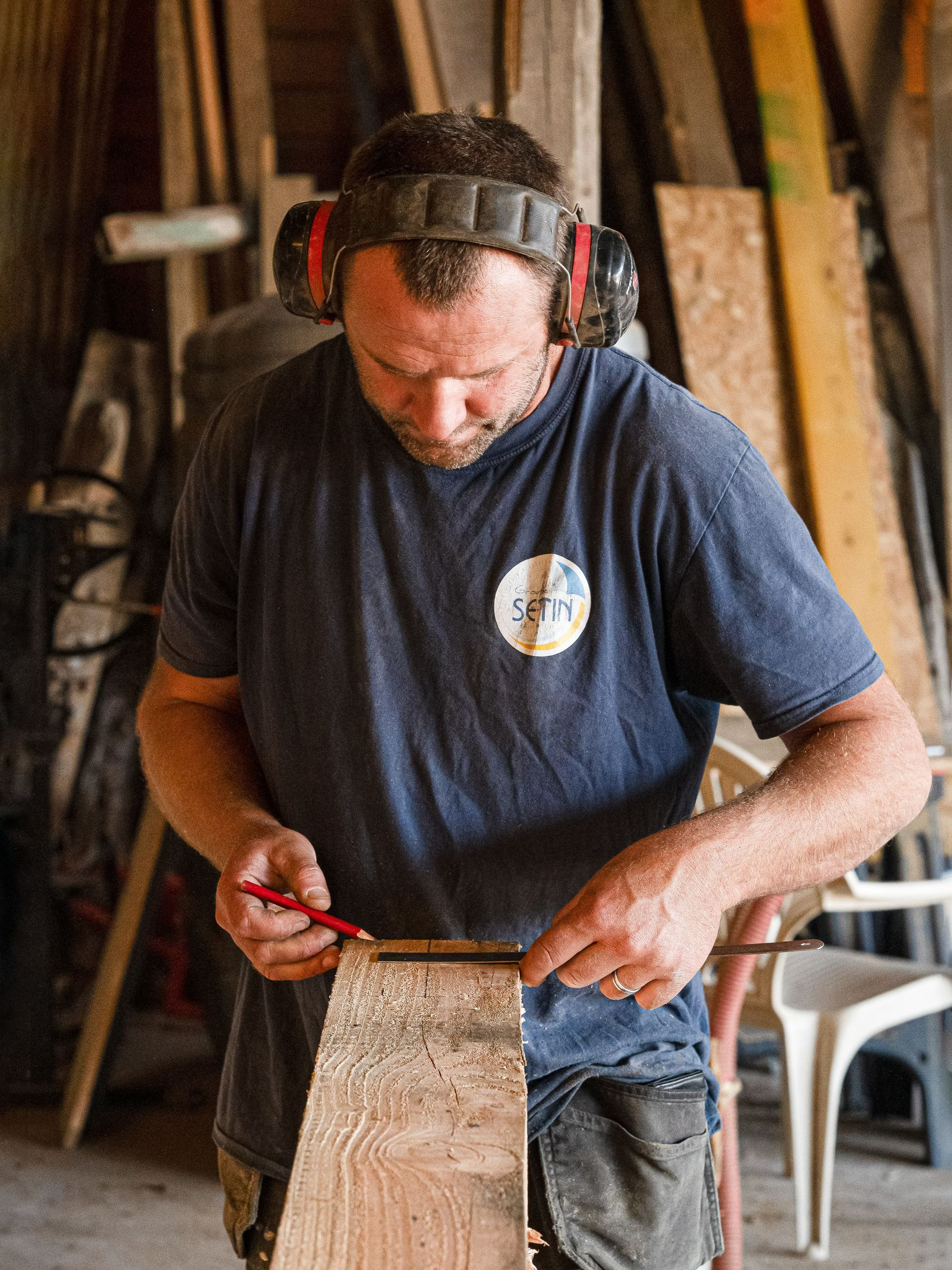 Un artisan consciencieux avec un casque anti-bruit sur la tête prend les mesures sur une poutre