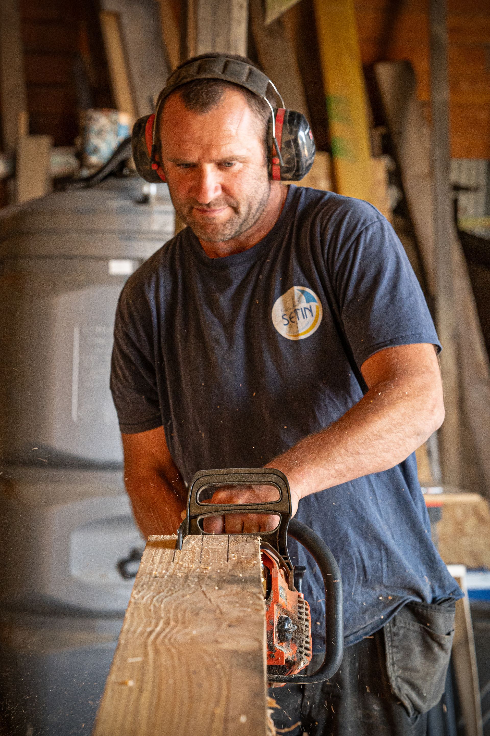 Jacob le charpentier qui coupe une poutre à l'aide d'une tronçonneuse