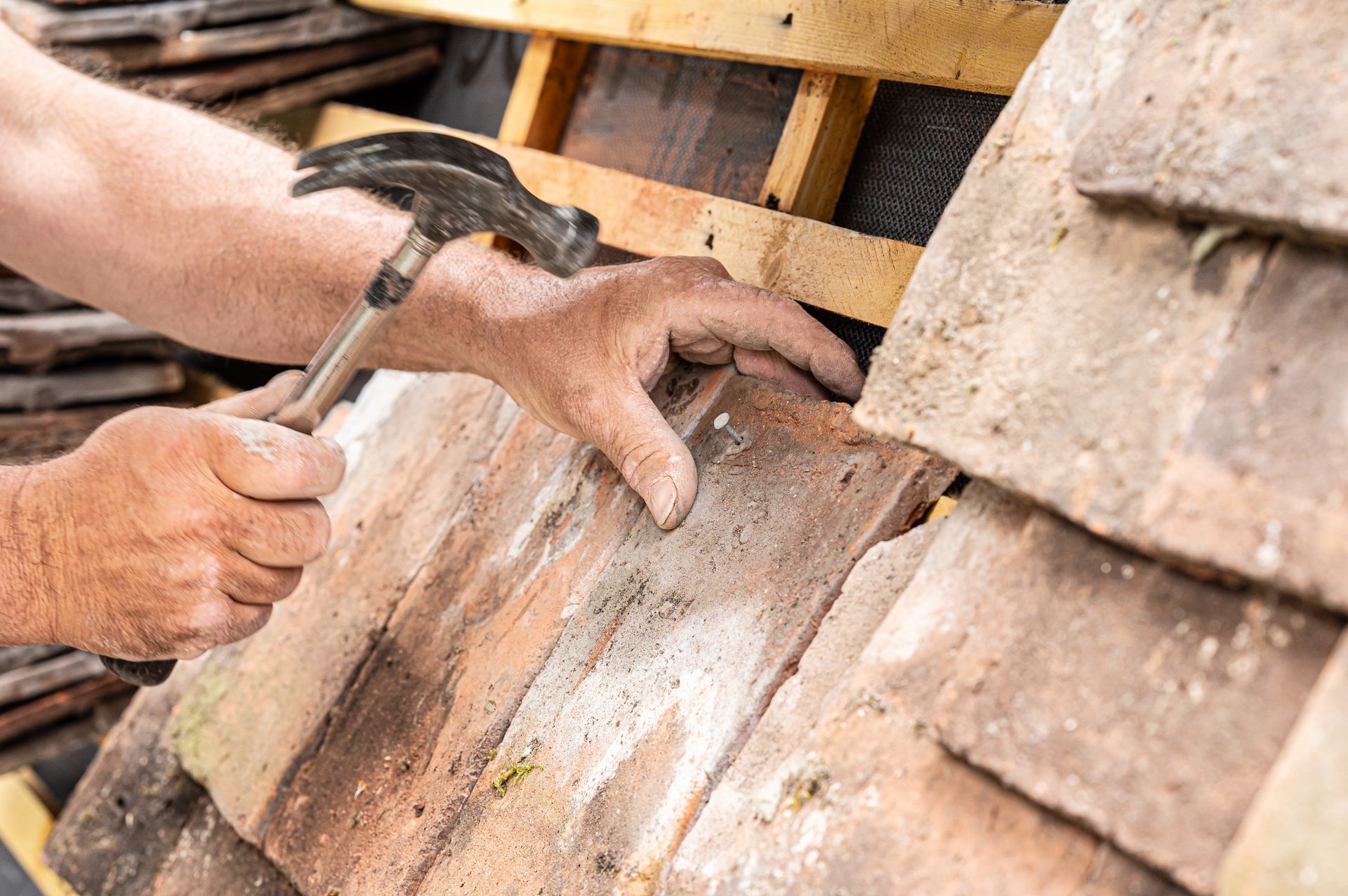 Gros plan sur les mains d'un artisan qui pose des tuiles sur une toiture ancienne
