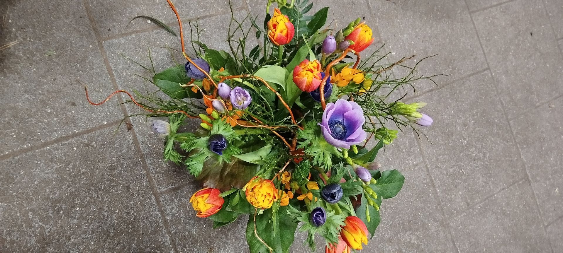 Hände arrangieren einen Brautstrauß aus tiefrosa Nelken, weißen Rosen und Eukalyptus auf einem Holztisch.