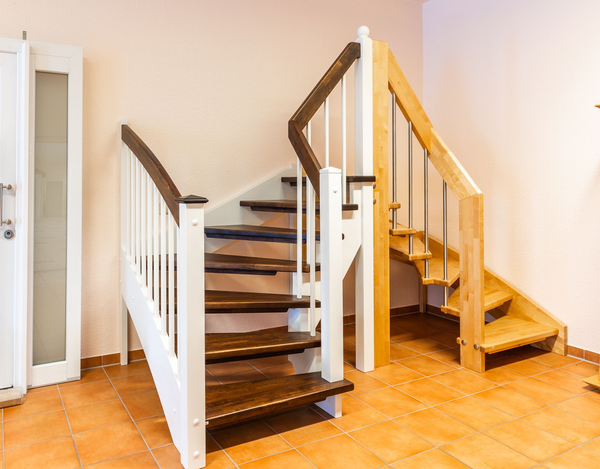 In einem Flur neben einer Tür befindet sich eine Holztreppe mit weißem Geländer.