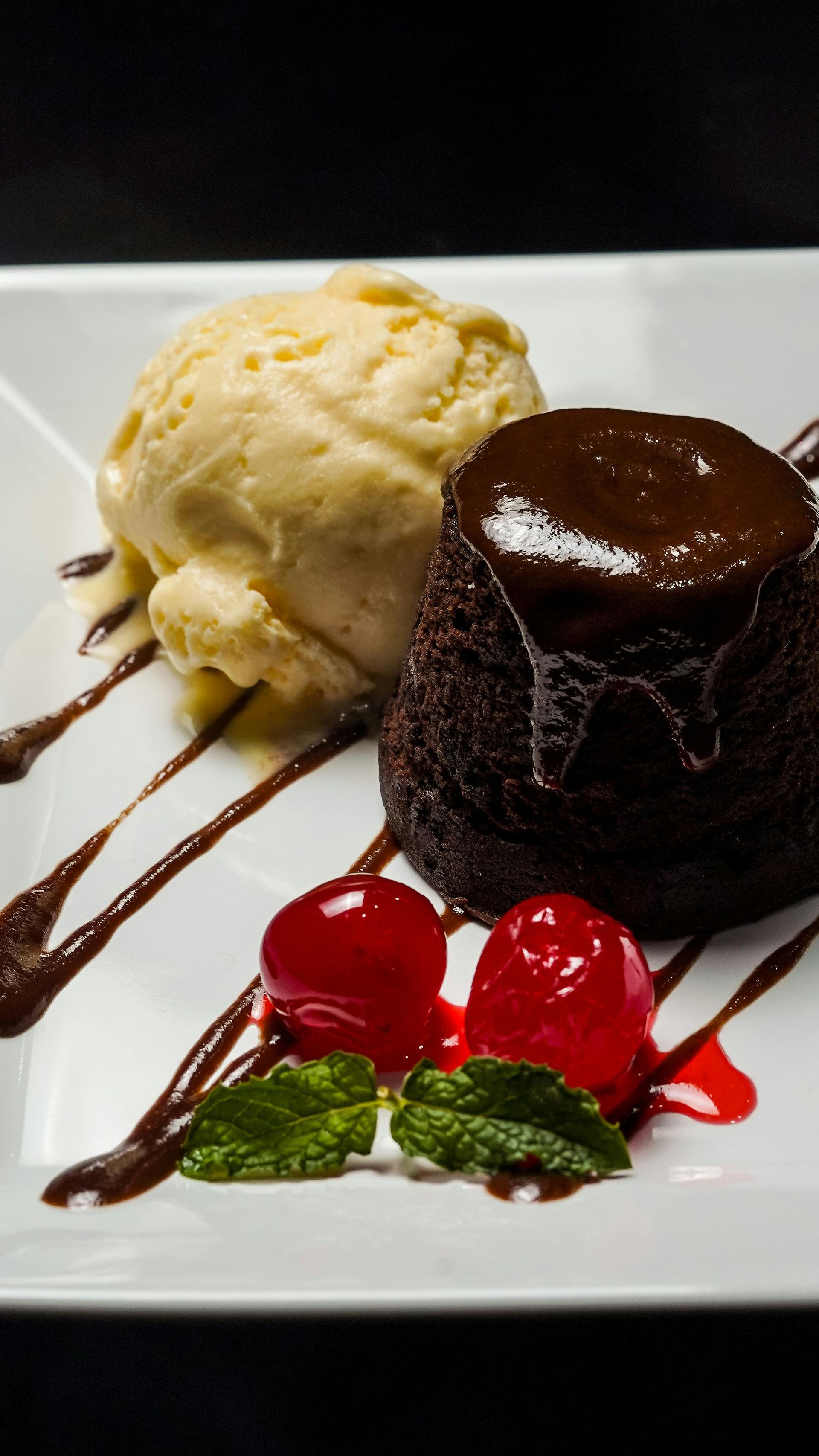 Pastel de chocolate fundido con helado de vainilla, sirope de chocolate y fresas en un plato blanco.