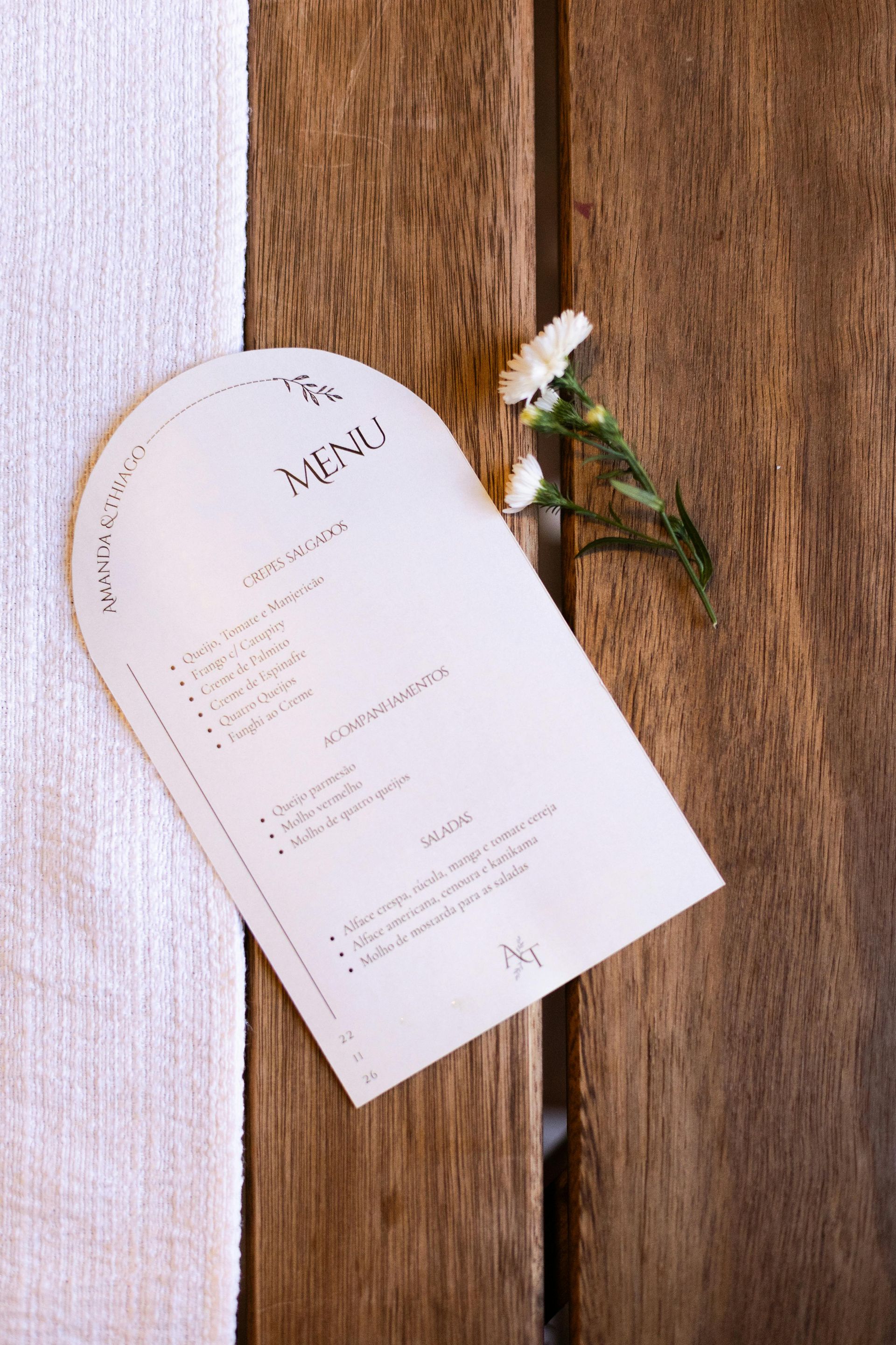 Tarjeta de invitación de boda blanca con una pequeña flor sobre fondo de madera.