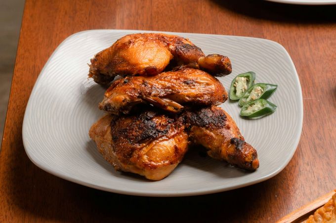 Plato de trozos de pollo asado con rodajas de pimiento verde sobre una mesa de madera.
