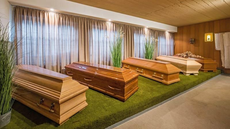 Vier Holzsärge stehen auf einem grünen Teppich in einem Raum.