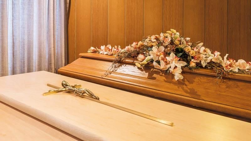 Ein Holzsarg mit Blumen und einem Kreuz darauf.