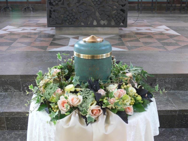 Eine grüne Urne ist von Blumen auf einem Tisch umgeben