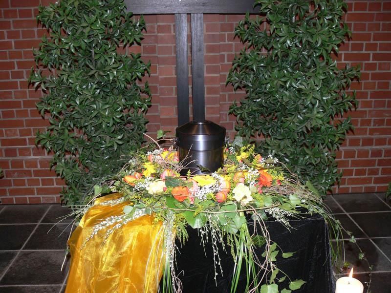 Eine schwarze Urne ist von Blumen und einer Kerze umgeben