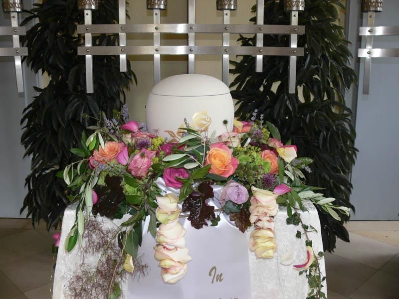 Eine weiße Urne steht auf einem Tisch, umgeben von Blumen
