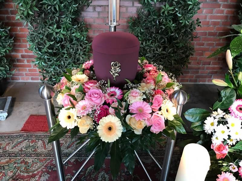 Eine violette Urne ist von rosa und gelben Blumen umgeben