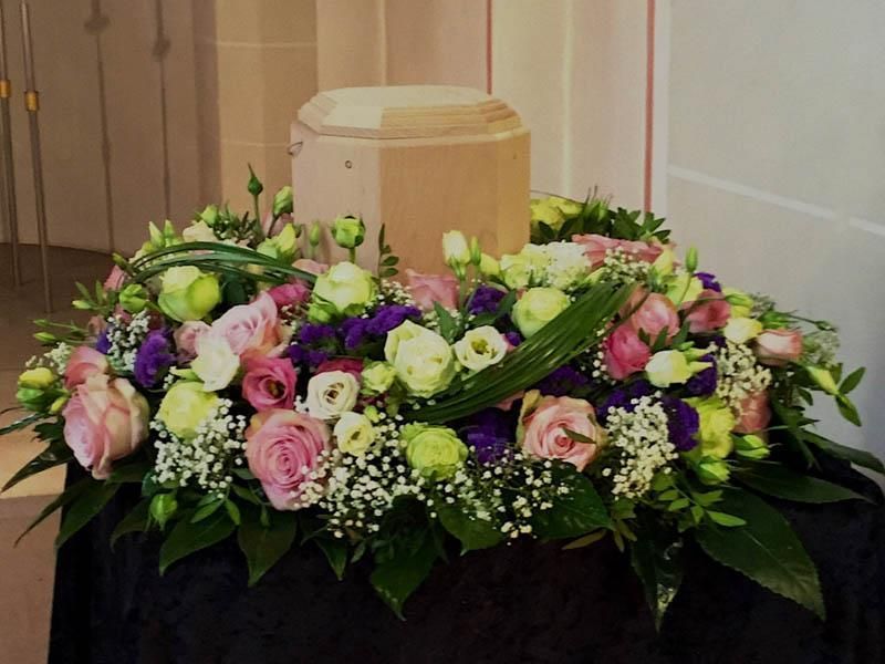 Eine Urne ist von rosa und lila Blumen umgeben