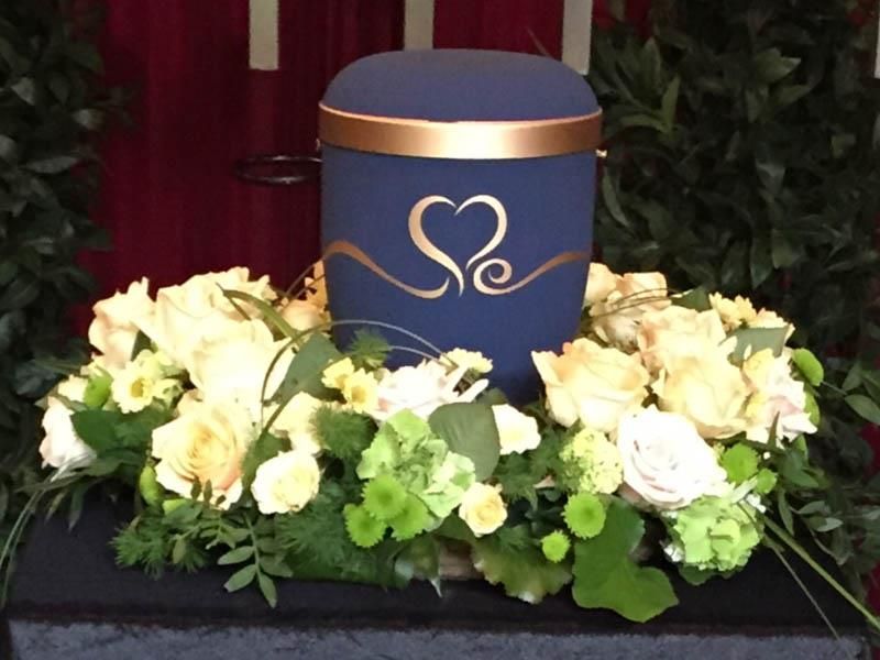 Eine blaue Urne mit einem Herz darauf ist von Blumen umgeben