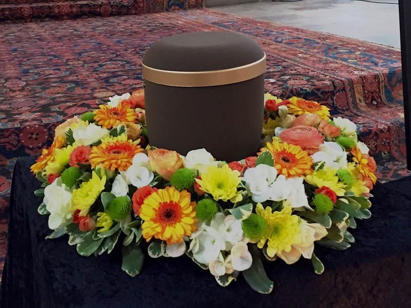 Eine schwarze Urne ist von einem Blumenkranz umgeben