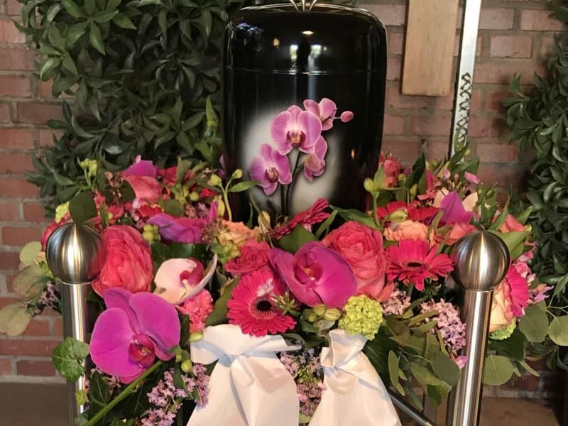 Eine schwarze Urne ist von rosa Blumen umgeben.