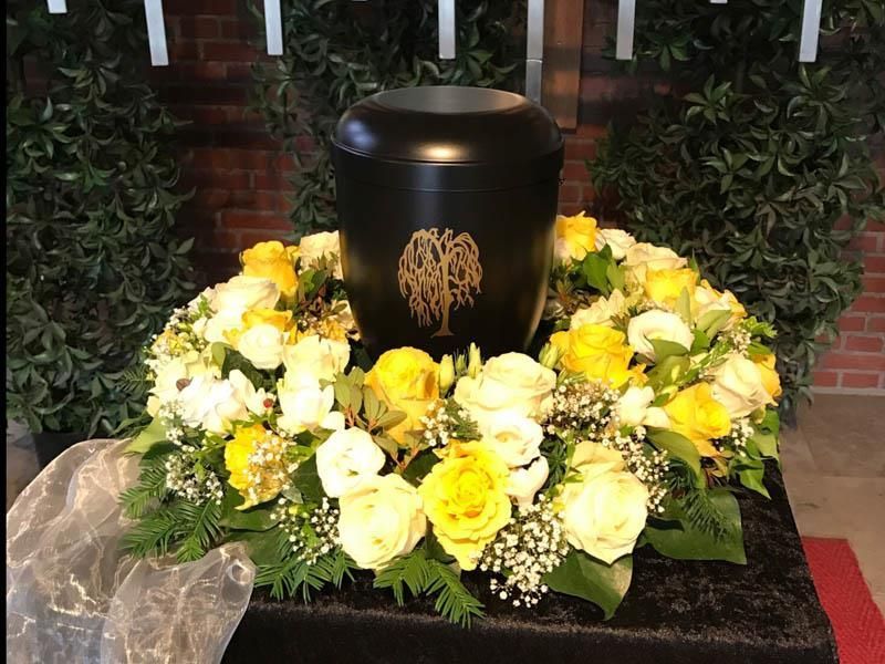 Eine schwarze Urne ist von gelben und weißen Blumen umgeben