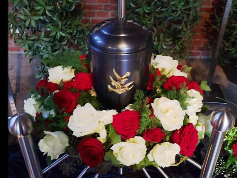 Eine schwarze Urne ist von roten und weißen Rosen umgeben