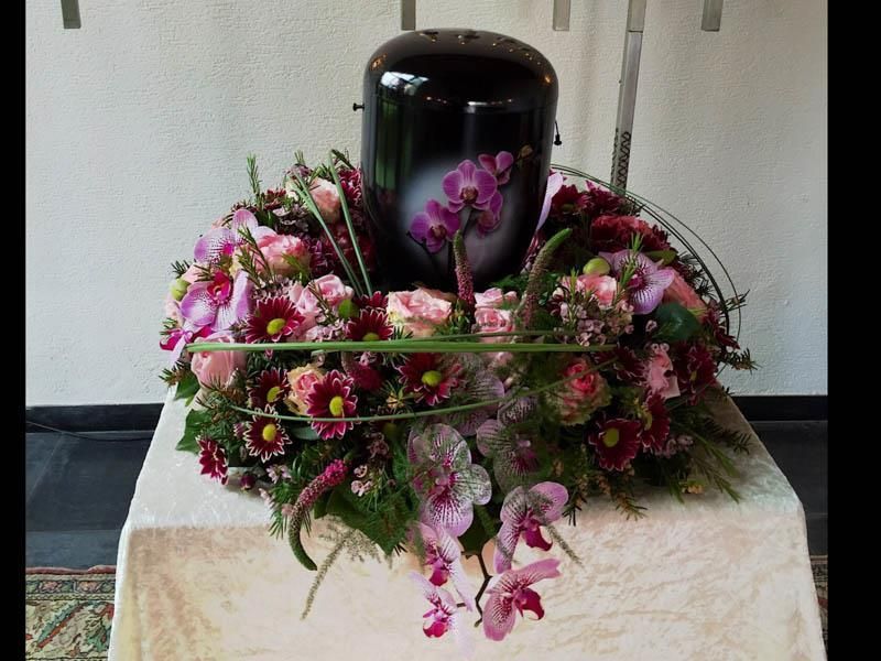 Eine schwarze Vase ist von Blumen auf einem Tisch umgeben