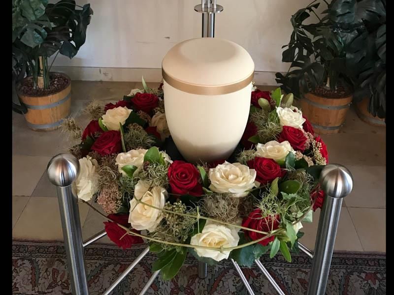 Eine weiße Urne ist von einem Kranz aus roten und weißen Rosen umgeben.