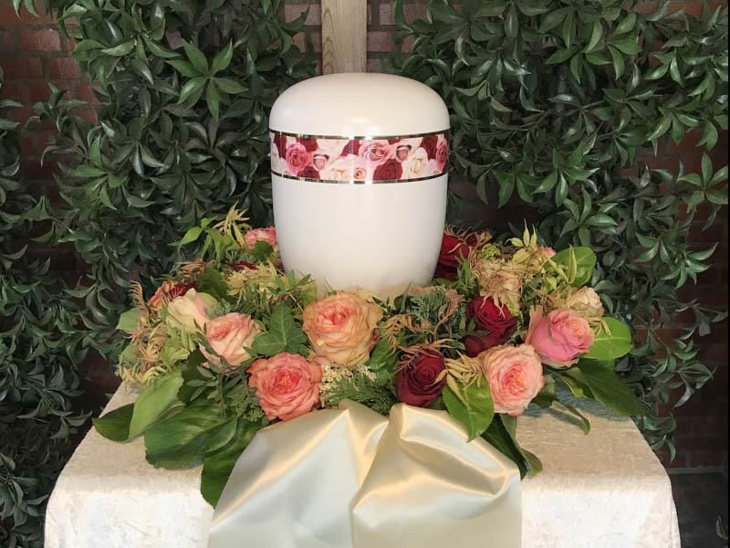 Eine weiße Urne ist von Blumen umgeben auf einem Tisch.