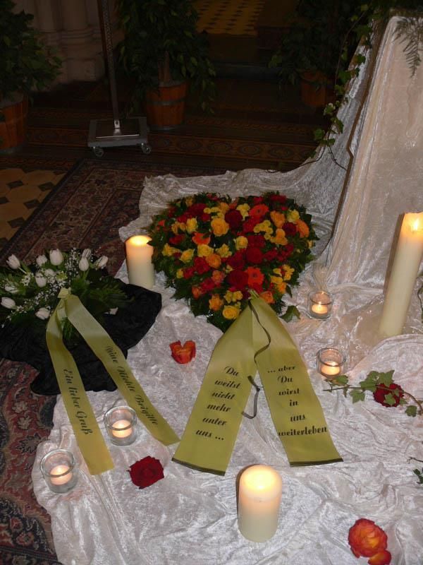 Ein herzförmiger Blumenstrauß ist von Kerzen und Bändern umgeben