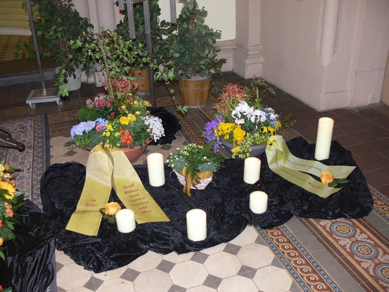 Ein Arrangement aus Blumen und Kerzen mit einer Schleife mit der Aufschrift 